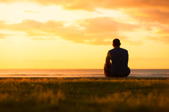 Silhouette of a person facing a calm sunrise over distant hills